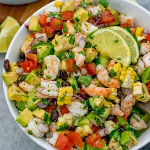 White bowl filled with salad that contains shrimp, avocados, tomatoes, onion, and various vegetables. All tossed with a cilantro lime dressing.