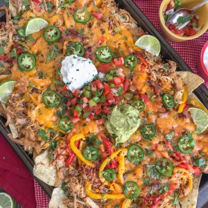 Loaded Chipotle Chicken Carnitas Nachos - more than likely the easiest, most flavor-packed nachos you will ever make! These nachos are loaded with chipotle chicken carnitas, salsa, cheese, sautéed onions and peppers, jalapeños, and topped with some amazing dips! #nachos #carnitas #loadnachos #mexican #tacotuesday #cincodemayo | https://withpeanutbutterontop.com