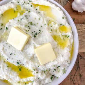 Garlic Parmesan Mashed Cauliflower - an easy, low-carb, healthier version of the traditional buttery, herb-filled mashed potatoes we all know and love! You won't even be able to taste the difference. #lowcarb #mashedcauliflower #cauliflowerpotatoes #healthy #sidedish | https://withpeanutbutterontop.com