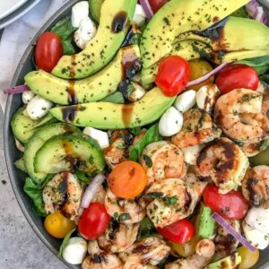 A light, refreshing salad that is perfect for any occasion. Loaded with fresh mozzarella, basil leaves, avocado slices, cherry tomatoes, cucumbers and tender shrimp - all tossed in a sweet balsamic glaze. Easy and bursting full of summertime flavors! #capresesalad #salad #shrimpsalad #summersalads | https://withpeanutbutterontop.com