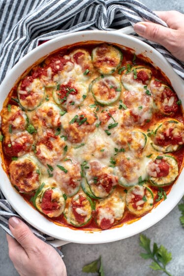 Baking dish filled with zucchini lasagna roll ups. Garnished with cheese and fresh seasonings. A great low-carb, gluten-free and healthy option to traditional lasagna.