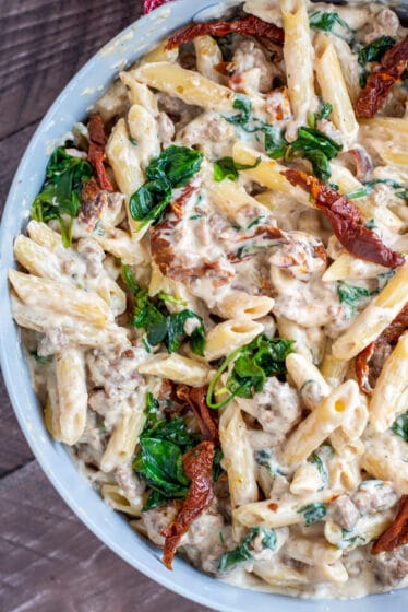 Bowl filled with creamy pasta, spinach, sun dried tomatoes, and turkey sausage.