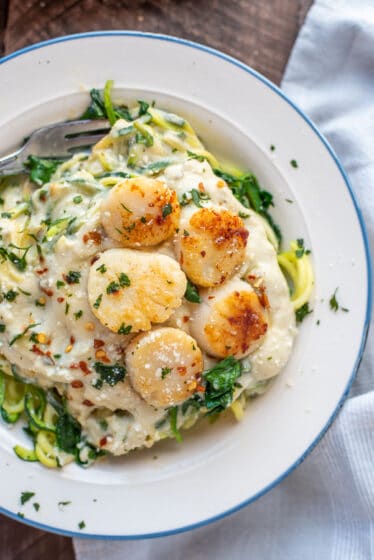 Close up photo of a white bowl filled with creamy zucchini noodles and garlic butter scallops.