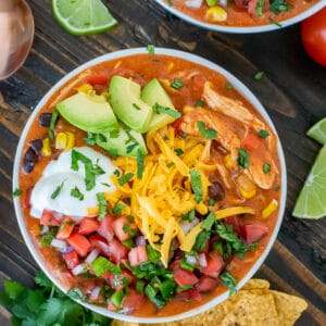 Bowl filled with chicken enchilada soup and garnished with avocado, greek yogurt, cheddar cheese and pico de gallo.