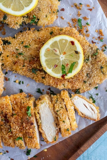 Platter with baked chicken breasts garnished with lemon slices.