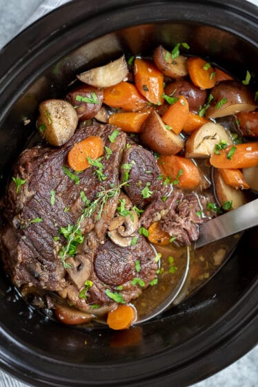 Crock pot filled with pot roast, potatoes, carrots, and mushrooms.