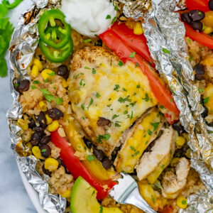 White plate with two grilled foil packets filled with veggies and chicken.