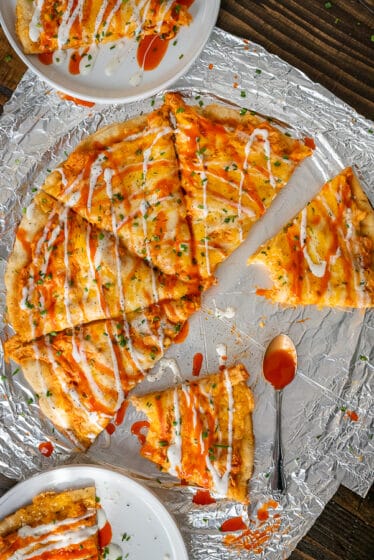 Buffalo Ranch Chicken Pizza sliced and garnished with buffalo sauce, ranch dressing and chopped chives.