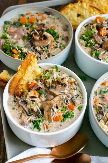 White bowls filled with creamy chicken and wild rice soup, garnished with cheese bread.