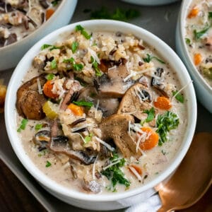 White bowls filled with creamy chicken and wild rice soup, garnished with cheese bread.