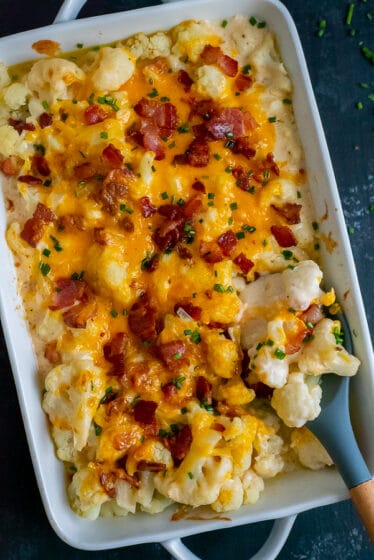 Casserole dish filled with creamy cauliflower topped with cheddar cheese, bacon, and chives.