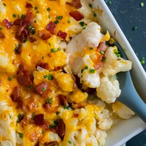 Casserole dish filled with creamy cauliflower topped with cheddar cheese, bacon, and chives.