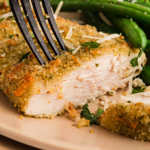 Crispy air fryer parmesan crusted chicken sliced on a white plate, served with green beans and buttered bread.
