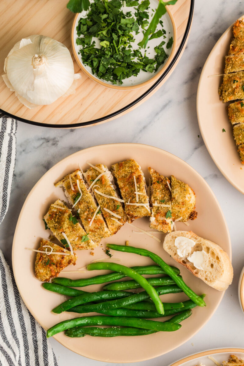 Plates filled with crispy parmesan chicken with green beans and buttered bread.