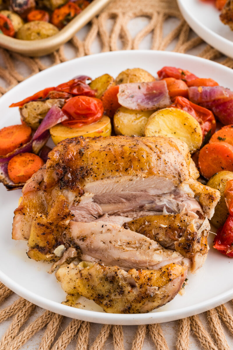 Photo of a white plate filled with roasted vegetables and crispy chicken thigh sliced open