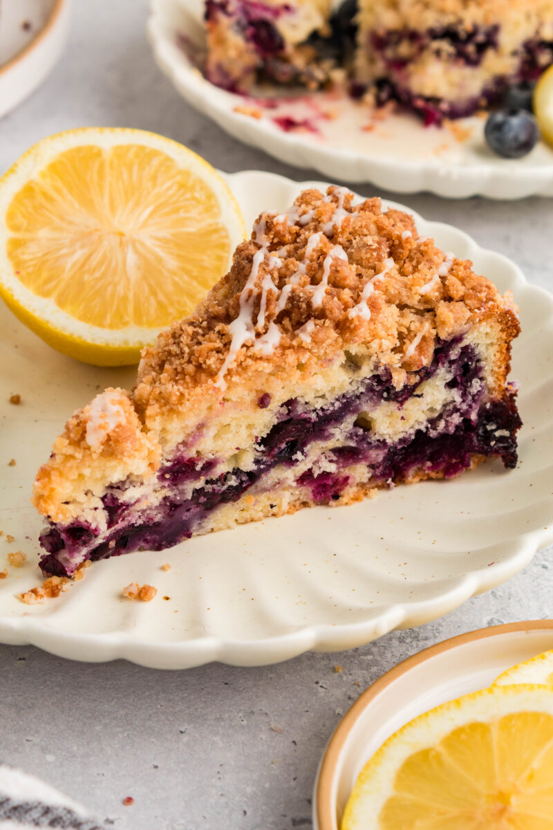 Lemon blueberry coffee cake with crumb topping and lemon glaze on a serving plate.